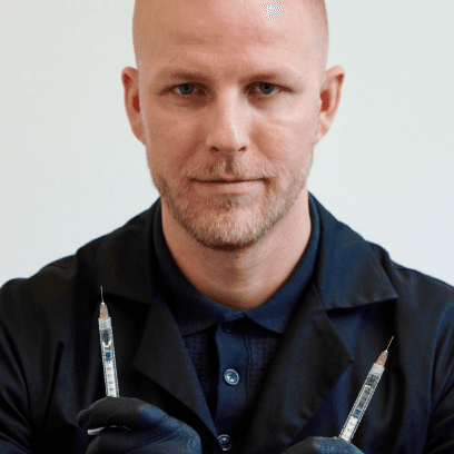 Dermatolog MUDr. Martin Bortlík drží v rukou dvě injekční stříkačky připravené pro estetické ošetření obličeje.