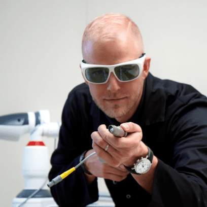 Dermatolog MUDr. Martin Bortlík má na očích ochranné brýle a v rukou drží laserový přístroj pro dermatologické ošetření.