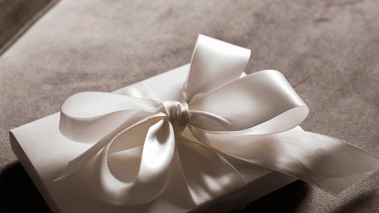 Elegantly wrapped gift with a large satin cream-colored ribbon, placed on a soft, velvety brown surface.
