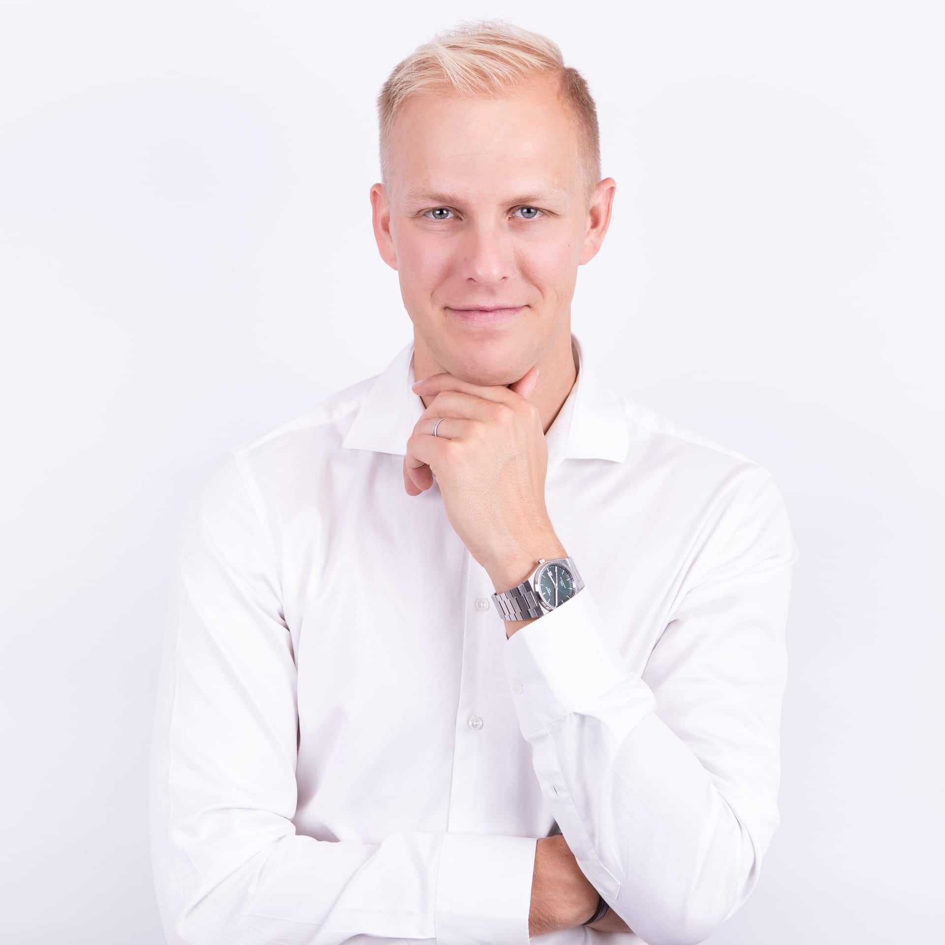 Portrait of MUDr. Martin Bortlík, dermatologist from Skinity Clinic, wearing a white shirt. He smiles and rests his chin on his hand, appearing friendly and professional.