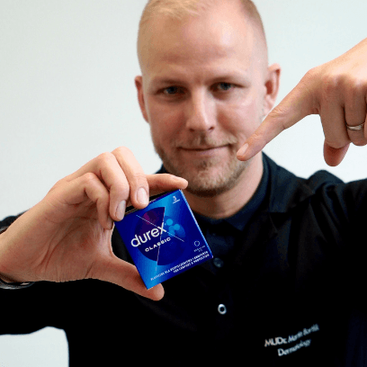 Dermatologist MUDr. Martin Bortlík holding a pack of condoms and pointing at it to illustrate sexual health screening awareness.