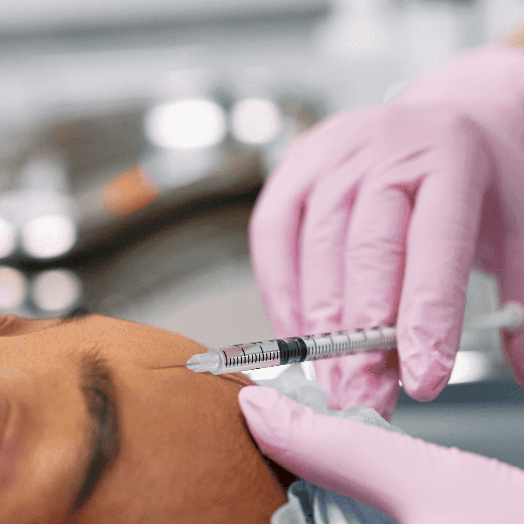 Kosmetička v růžových rukavicích aplikuje injekci botulotoxinu do oblasti čela ženy ležící během estetického ošetření pleti.