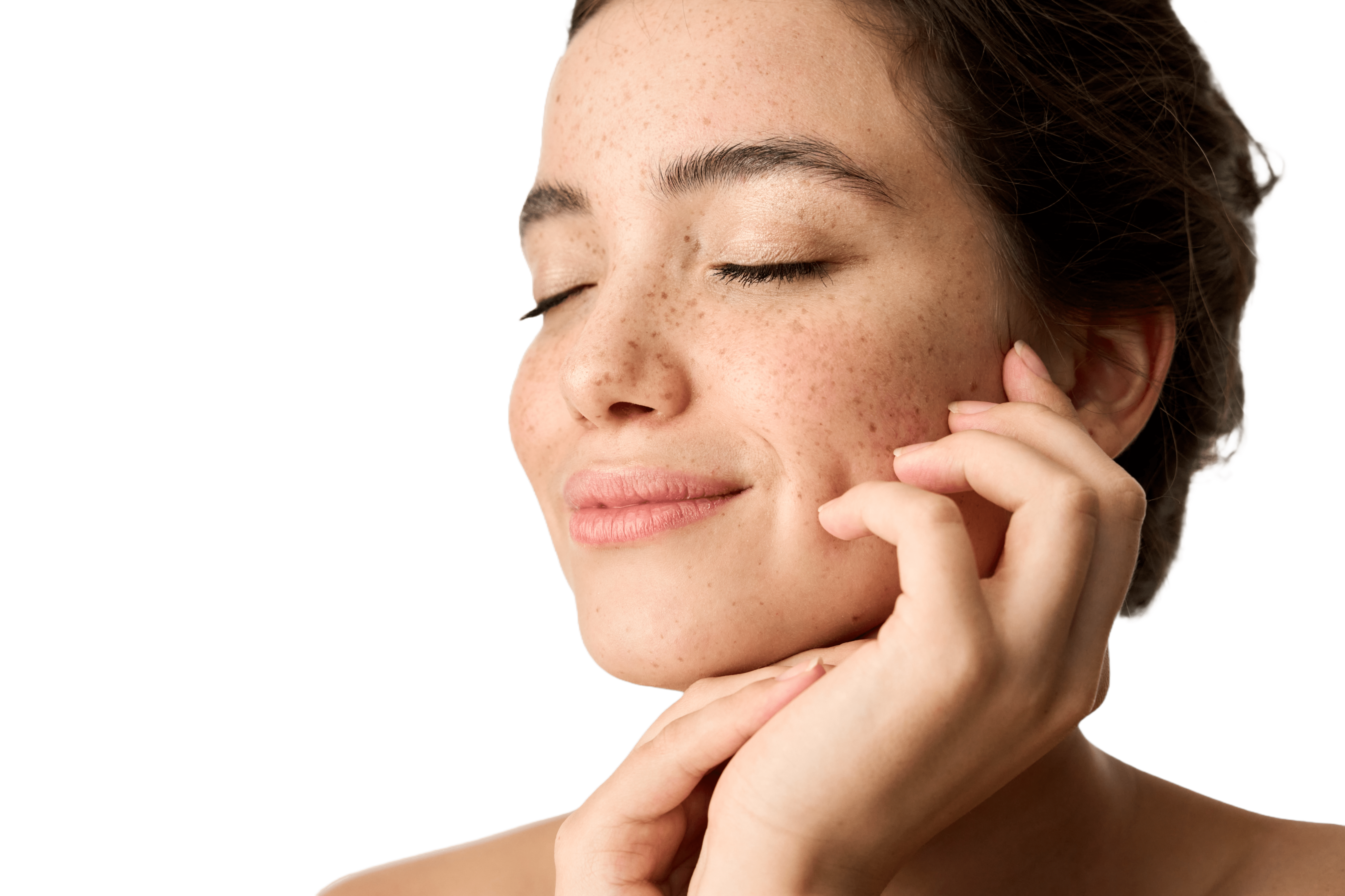 Portrét mladé ženy s pihami a zavřenýma očima – jemně se usmívá a dotýká se své tváře. Působí klidně a přirozeně a je osvícena měkkým světlem.